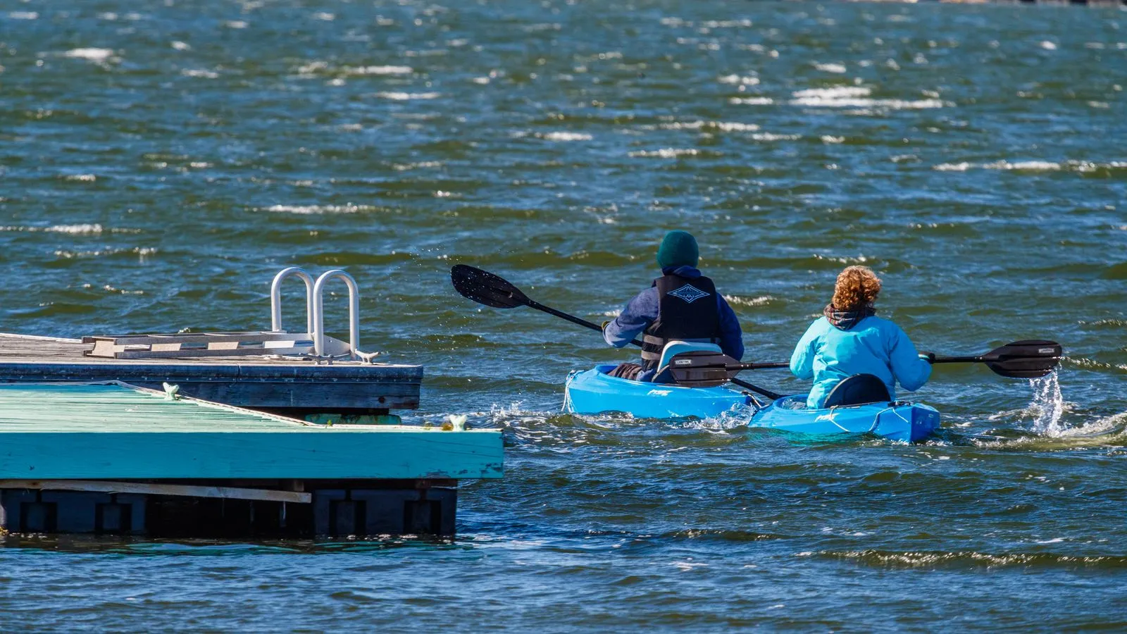 Two people kayaking on a sunny day near a dock, enjoying leisure time on the water.